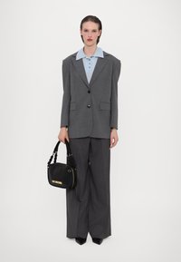 Gray pinstriped oversized blazer layered over a blue collared shirt, paired with wide-leg gray trousers and a black handbag with gold lettering.