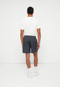 Men's grey shorts with white piping, elastic waistband, and a back pocket, paired with a plain white t-shirt and white sneakers.