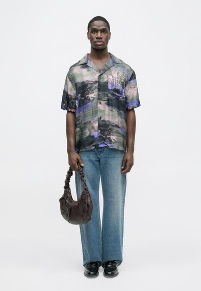 Majica s kratkimi rokavi v večbarvnih abstraktnih vzorcih, kombinirana s svetlo modrimi kavbojkami širokih nog in temno rjavo torbico za čez ramo.