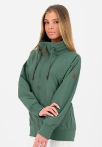 Grøn zip-up jakke lavet af letvægtsstof, med en høj krave, justerbar snoretræk og ribbede manchetter og kant.