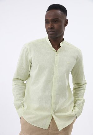 Camisa de color verde claro con cuello y acabado texturizado, que cuenta con un cierre de un solo botón y un pequeño logo. Mangas largas, dobladillo circular.