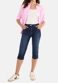 Vaaleanpunainen pitkähihainen paita, valkoinen toppi, tummansiniset polveen ulottuvat farkkuröyhelöt ja valkoiset tennarit mustilla yksityiskohdilla.