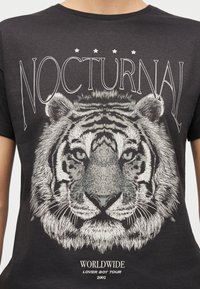 Κοντινό πλάνο μαύρου T-shirt με λεπτομερή άσπρο πρόσωπο τίγρης, το κείμενο «NOCTURNAL» πάνω και «WORLDWIDE LOVER BOY TOUR 2002» κάτω.