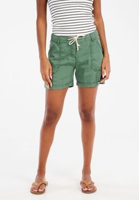 Groene katoenen shorts met opgerolde omzomen, zijzakken en een verstelbare trekkoord taille, gecombineerd met een gestreepte mouwloze top en sandalen.