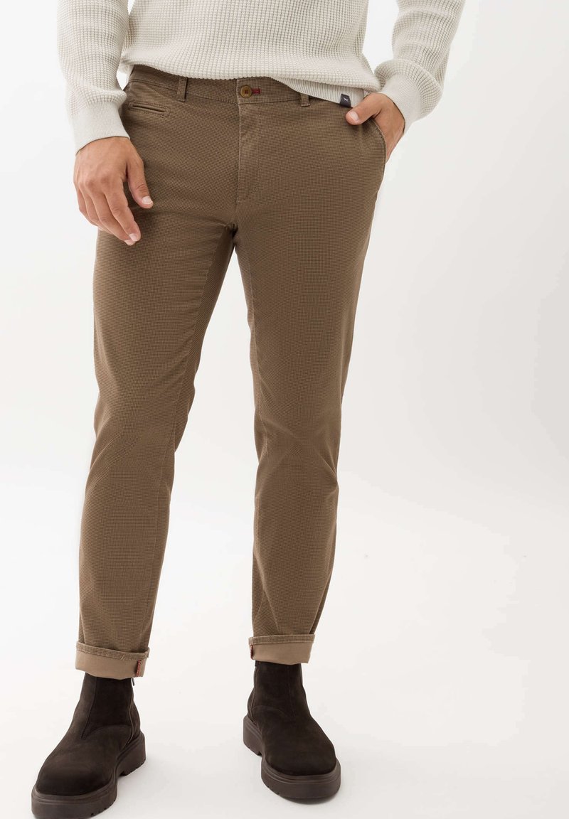 Bruine, gestructureerde broek met een slim fit, voorzien van een opgerolde zoom en een enkele knoopsluiting, gecombineerd met donkere suède enkellaarsjes.