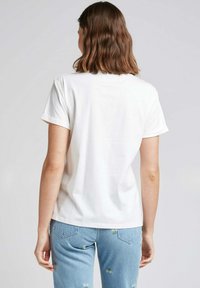 T-shirt en coton blanc avec des manches retroussées, affichant une texture douce. Associé à un jean bleu clair avec des accents floraux brodés.