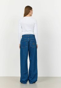 Jeans din denim cu picioare largi, într-o nuanță de albastru închis, cu talie înaltă, dotate cu două buzunare pe spate și un detaliu subtil cu logo. Material din bumbac texturat.