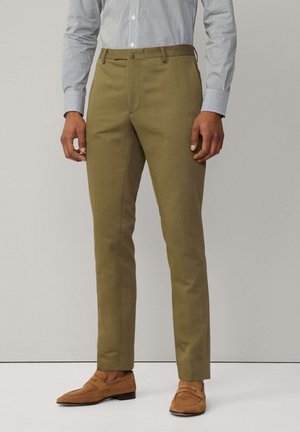 Pantalons ajustés vert olive avec une finition de tissu lisse, design slim fit et poches standard, associés à des mocassins en suède marron.