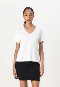 Hvit bomulls T-skjorte med V-hals og korte ermer, med en avslappet passform. Kombinert med et svart denimskjørt. Glatt tekstur, minimalistisk design.