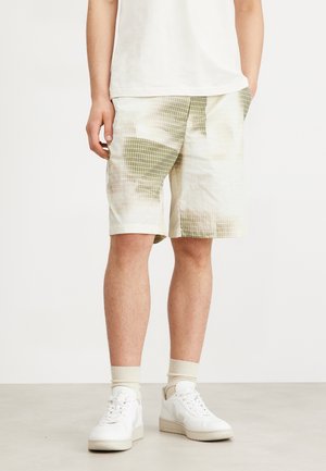 Light-colored shorts made from textured fabric with a grid pattern in green. Features side pockets and a relaxed fit. Worn with white sneakers.