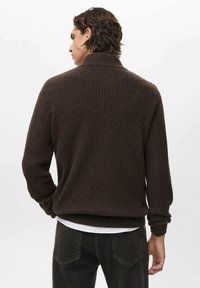 Maglione a coste, marrone scuro, con colletto alto e maniche lunghe. Realizzato in tessuto morbido, presenta una vestibilità comoda e dettagli minimi.
