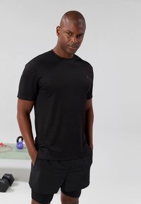 T-shirt atlética preta em tecido liso com decote redondo, combinada com calções pretos. Design simples com detalhe de marcação minimalista.