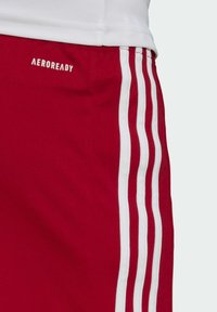Red athletic shorts with white stripes along the sides. Features "AEROREADY" logo in white. Made of a smooth, breathable fabric.
