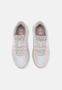 Scarpe sportive grigie con tomaia in mesh e accenti testurizzati, dotate di lacci rosa chiaro e suola beige. Logo Under Armour sulla linguetta.