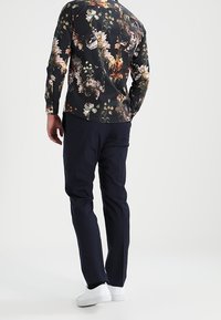 Bloemenprint overhemd met lange mouwen en zwarte ondergrond, voorzien van levendige kleuren; gecombineerd met marineblauwe broek en witte sneakers, een casual outfit.