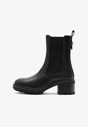 Bottine en cuir noir avec des panneaux latéraux élastiques, bout rond et talon bloc texturé. Coutures détaillées et languette à l'arrière.