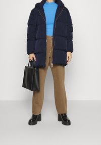 Námořnicky modrá prošívaná bunda s kapucí a předním zipem, doplněná modrým žebrovaným topem, hnědými kalhotami a černými platformovými botami. V ruce černá kabelka typu tote.