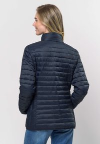 Tamsiai mėlyna pūkinė striukė su aukštu apykakliu, horizontaliu siuvimu ir lygiu, blizgiu paviršiumi. Modelis parodytas iš nugaros.