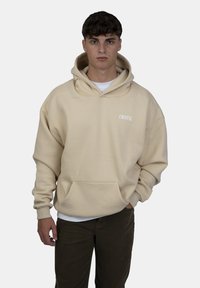 Overgrote beige hoodie met een voorzak en een trekkoordcapuchon, met daarop witte "CRYSTAL" tekst op de borst. Zachte, gestructureerde stof.
