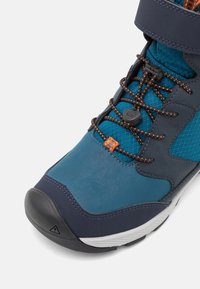 Blaue und marineblaue Wanderschuhe aus strukturiertem Leder und Mesh. Mit orangen Schnürsenkeln und einer Gummi-Zehenkappe. Klettverschluss am Knöchel.