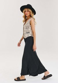 Bežová bezrukávová vestu s kvetinovým vzorom v kombinácii s voľnými čiernymi maxi sukňami. Čierny klobúk so širokým okrajom a tmavohnedé sandále s uzlom dotvárajú celkový vzhľad.