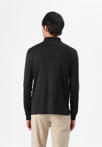 Camisa negra de manga larga con cuello clásico, textura suave y diseño ajustado. Presenta una espalda lisa sin adornos.