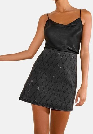 Mujer que lleva un top sin mangas de satén negro y una falda corta oscura con un patrón de diamantes y detalles sutiles y brillantes.
