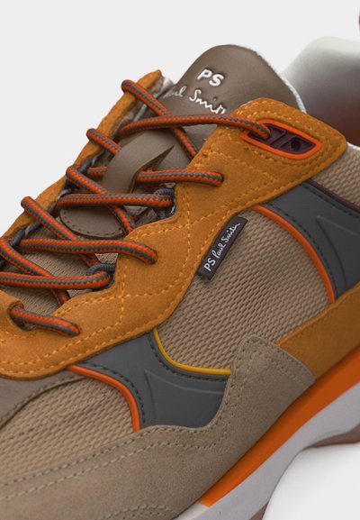 Κοντινό πλάνο καφέ και πορτοκαλί αθλητικού παπουτσιού με ύφασμα διχτυωτό, επικαλύψεις από δέρμα σουέντ, κορδόνια με σχέδια και λογότυπο "PS Paul Smith" στη γλώσσα και στην πλαϊνή ταμπέλα.