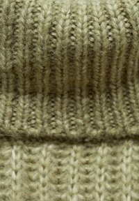 Stickad tyg i dämpad olivgrön färg med ett texturerat ribbmönster med varierande stygnstorlekar, mjuk och fluffig textur genom hela ytan.