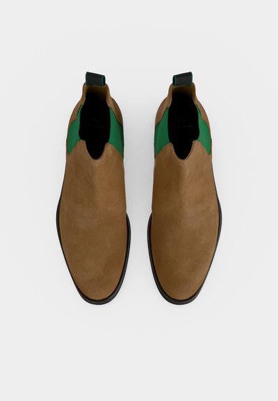 Ζευγάρι καφέ σουέντ μποτάκια slip-on με πράσινα ελαστικά πλευρικά πάνελ και μαύρες σόλες, εμφανιζόμενα από πάνω σε απλό φόντο.