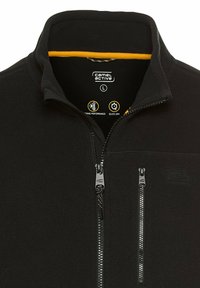 Zwarte fleece jas met hoge kraag, ritssluitingen op de zakken en grijze hardware. Heeft een gele binnenvoering en merklogo op de kraag.