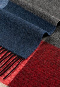 Wool scarf featuring a red and grey plaid pattern, with navy and grey accents, fringe detail on one edge, and a soft, textured surface.