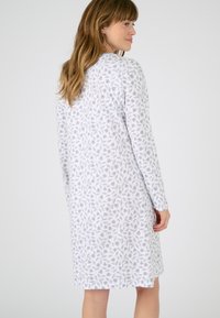 Camisa de noche de manga larga en blanco con un patrón floral gris. Tejido suave, longitud hasta la rodilla, escote redondo y corte relajado.