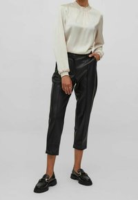Blouse en satin crème avec col froncé, associée à un pantalon noir en similicuir court. Mocassins noirs avec des accents dorés complètent le look.