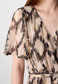 Vestido impreso con tejido suave y ligero en beige con manchas de leopardo en marrón y negro; mangas cortas con vuelo y diseño en forma de v.