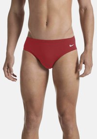 Costume da bagno rossi in tessuto elasticizzato, con un design a vita bassa e un logo Nike bianco sul lato sinistro. Texture liscia.