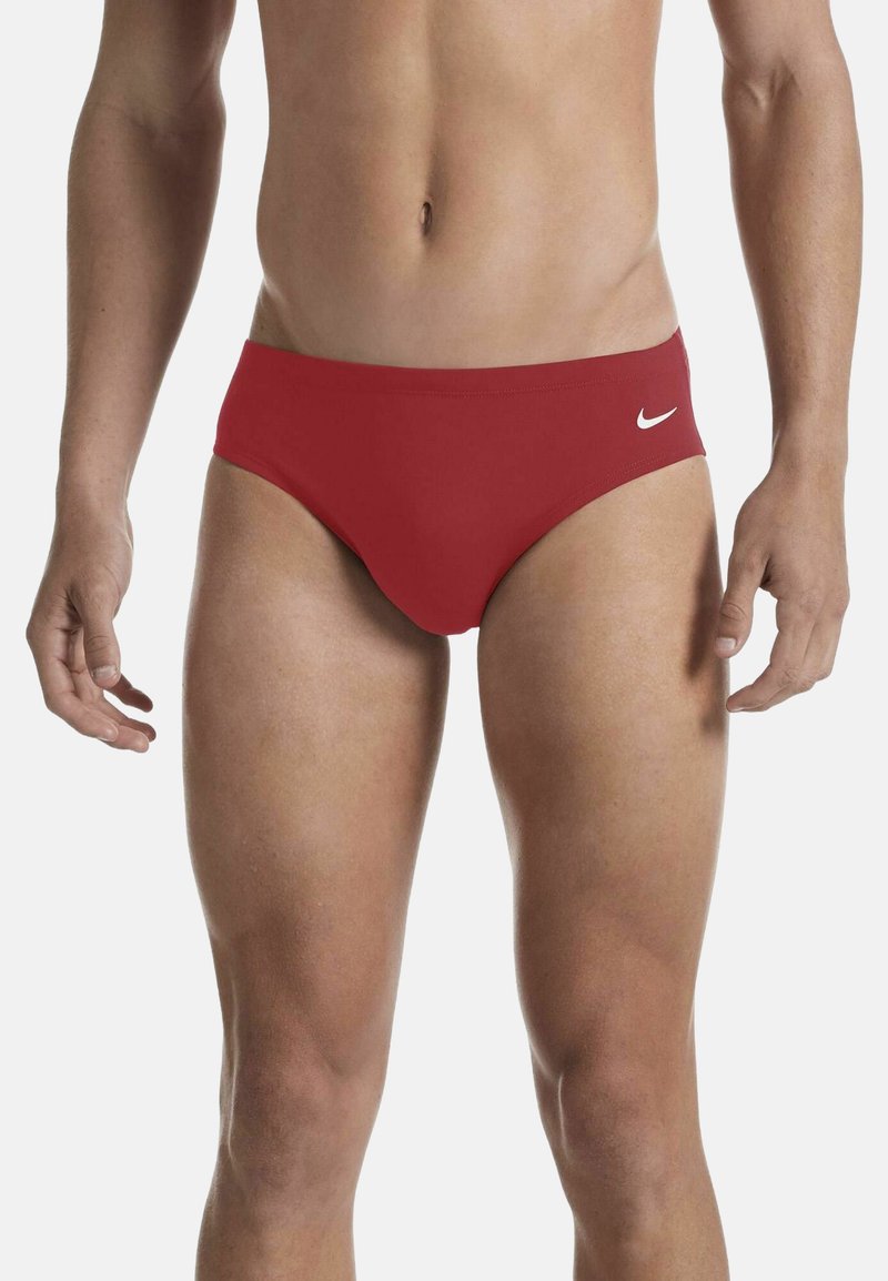 Costume da bagno rossi in tessuto elasticizzato, con un design a vita bassa e un logo Nike bianco sul lato sinistro. Texture liscia.
