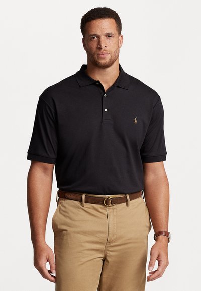 Schwarzes Poloshirt aus atmungsaktivem Stoff mit einer Drei-Knopf-Leiste und Logosstickerei. Kombiniert mit khakifarbenen Hosen und einem braunen Gürtel.