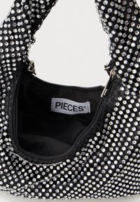 Fekete kézitáska, textúrált felülettel, ezüst színű strasszokkal borítva. Cipzáros nyitással és "PIECES" feliratú címkével rendelkezik.