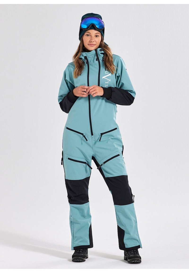 Een teal en zwarte skikostuum met een ritssluiting aan de voorkant, meerdere zakken en een comfortabele pasvorm. Voorzien van een hoge kraag en verstelbare manchetten.