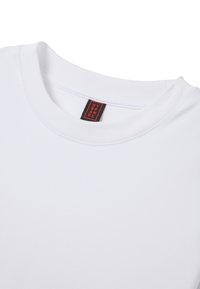 T-shirt bianca a girocollo con un primo piano del colletto e un'etichetta di marca rettangolare nera e rossa cucita all'interno.