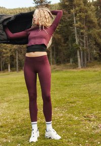 Dopasowany top sportowy i legginsy w kolorze burgundowym o gładkiej fakturze. Strój ma krótki fason i jest zestawiony z białymi butami sportowymi.