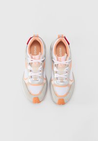 White and orange athletic sneakers with mesh, suede, and silver accents. Features thick soles, laces, and a logo on the insole.