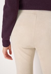Leggings beige, con texture e design aderente, sono abbinati a un maglione in maglia di un viola scuro. Il tessuto appare morbido e liscio.