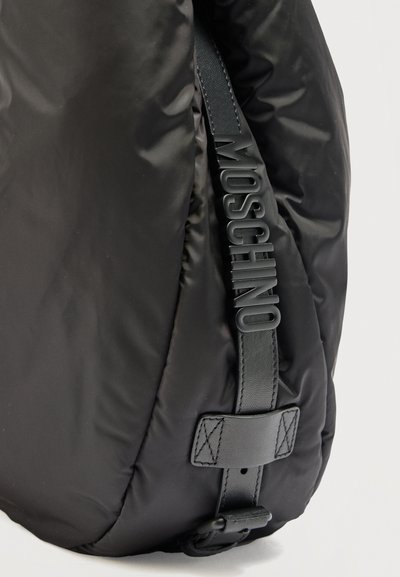 Μαύρη επενδυμένη υφασμάτινη τσάντα με κάθετο μαύρο δερμάτινο λουράκι με ανάγλυφο το όνομα της μάρκας "MOSCHINO" σε ανάγλυφα γράμματα.