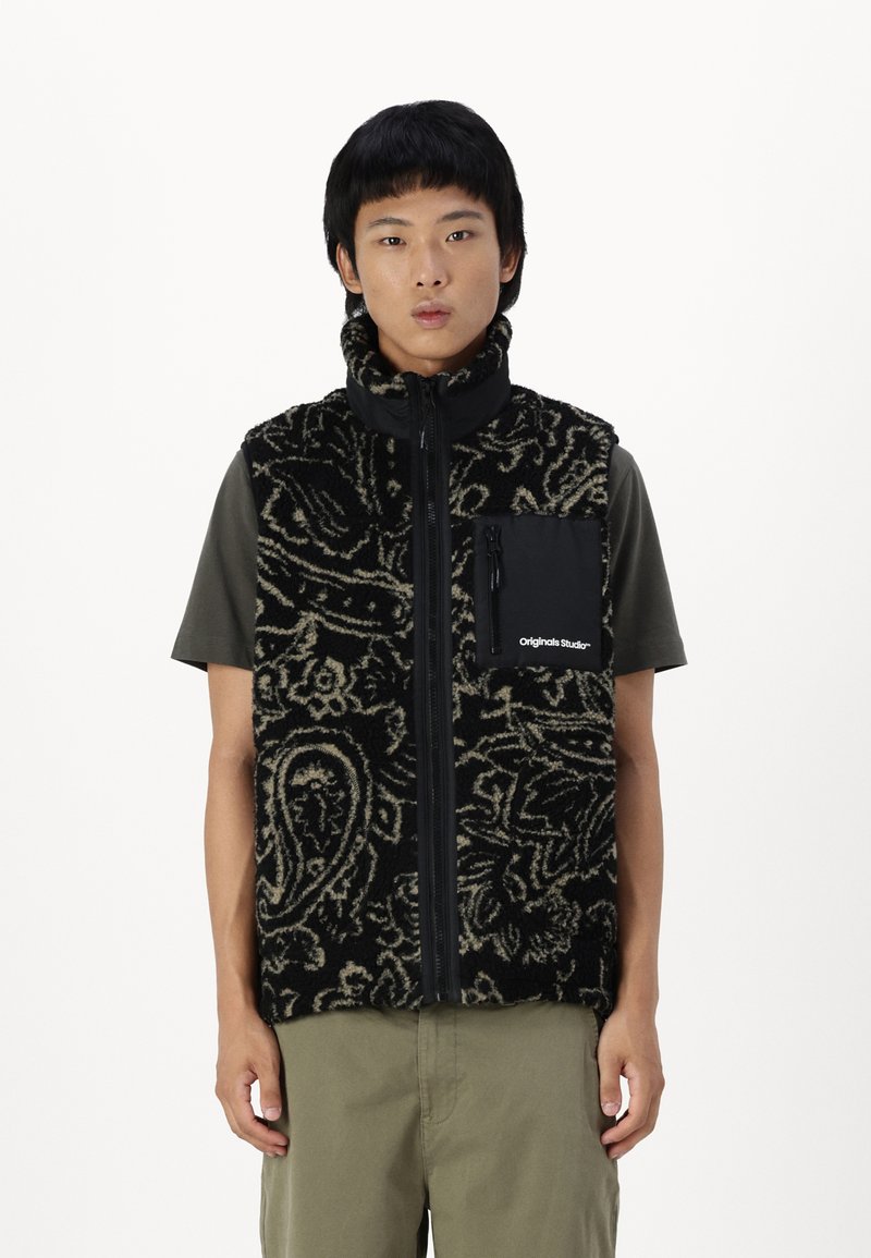 Black fleece vest with intricate beige patterns, featuring a high collar, zip closure, and a black pocket with a logo on the chest.
