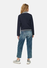 Navy blue jacket with a white striped collar, paired with light blue denim jeans. The outfit features a relaxed fit and casual sneakers.