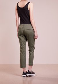 Chinos vert olive avec une coupe slim et une longueur cheville. Poches arrière avec un subtil détail de couture. Associés à des chaussures à plateforme noires.