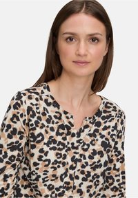 Bluse mit Leopardenmuster in Beige, Schwarz und Braun, aus leichtem Stoff, V-Ausschnitt und dezenten Falten an den Schultern.