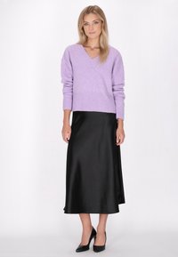 Lavendelfarbener Strickpullover mit V-Ausschnitt und geripptem Saum, kombiniert mit einem schwarzen Satin-Maxikleid und schwarzen High-Heels.